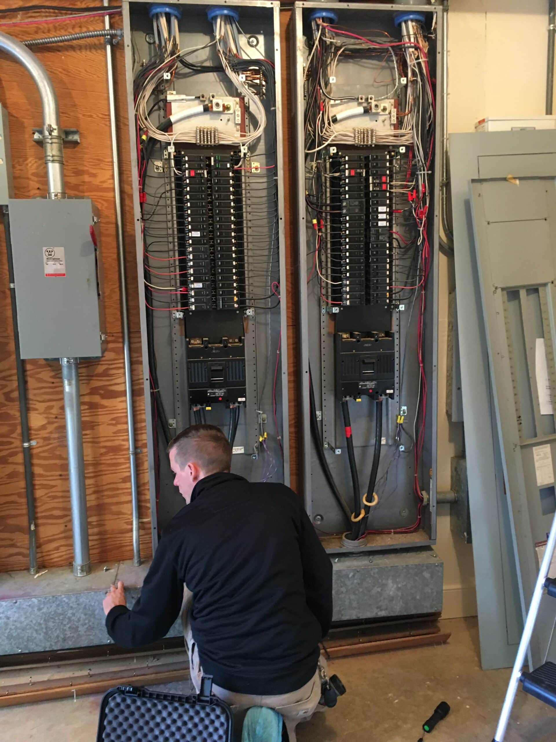 A home inspector crouching in front of two electrical panels.